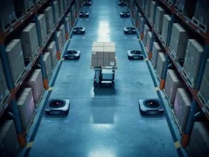 Autonome magazijnrobots rijden door brede gangpaden tussen hoge metalen stellingen vol kartonnen dozen, luchtperspectief.