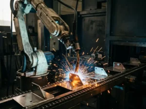 Robotarm last metaalonderdelen op een lopende band, met vonken en dramatisch blauw-amberkleurig industrieel licht.